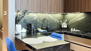 A modern kitchen with a black marble countertop, two blue chairs, a sink, and a stove. - Nest One (Tashkent)