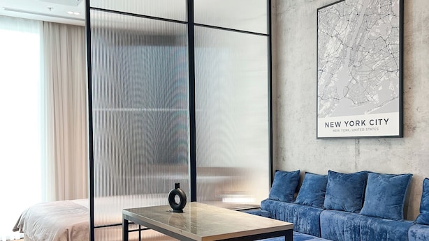 A modern hotel room with a bed, a sofa, a small table, a decorative vase, a map on the wall, and a window with curtains. - Nest One (Tashkent)