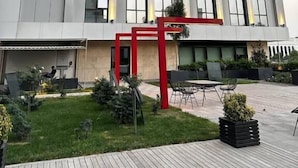 A modern building with a large glass facade, a red entrance structure, and a well-maintained outdoor area with seating and plants. - Nest One (Tashkent)