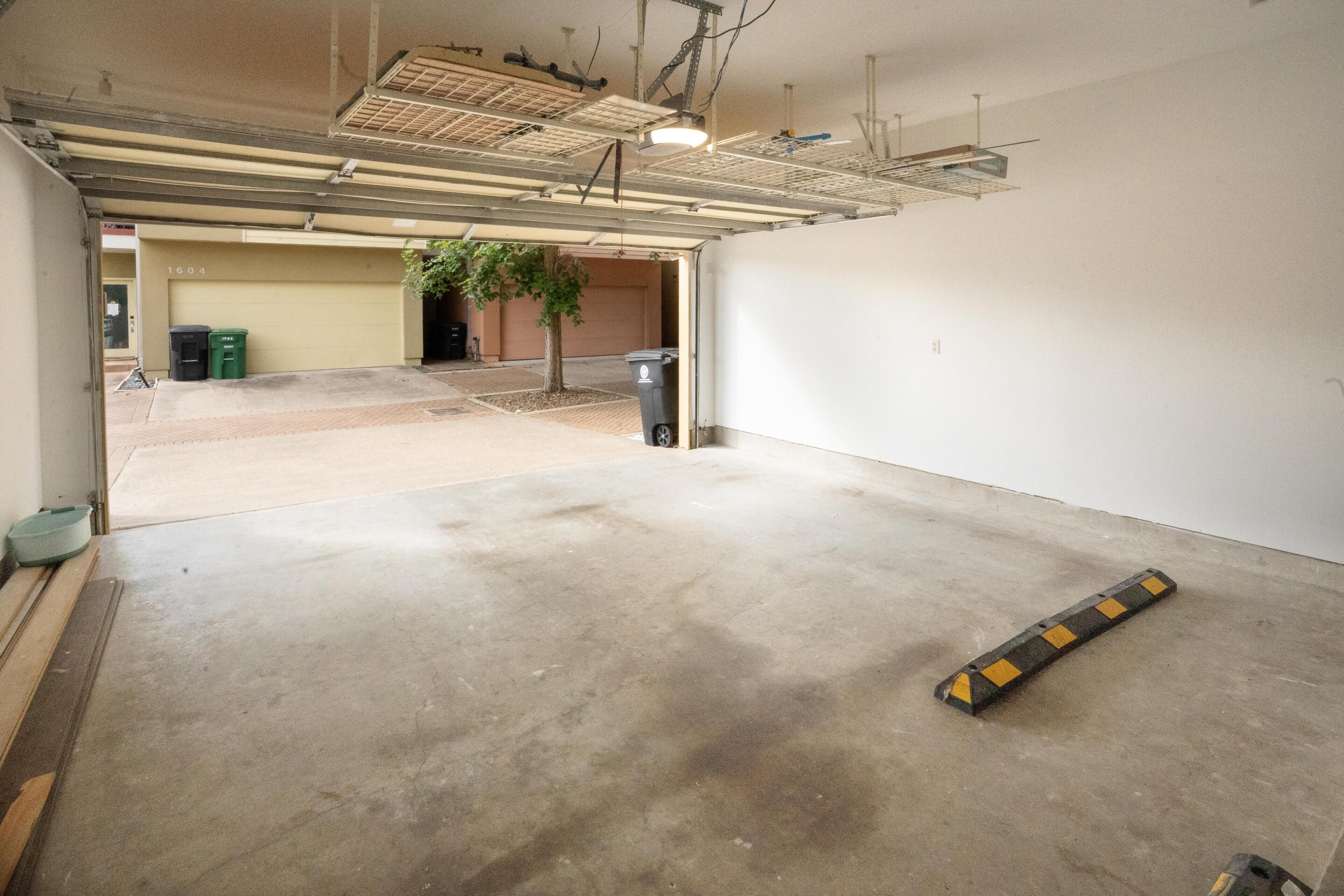 Un vaste espace de stationnement intérieur doté d’un sol en béton, d’un arbre et de quelques poubelles.