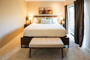 A bedroom with a large bed, a bench, two bedside tables with lamps, a painting on the wall, and a window with curtains. - 3-bedroom, 4-bed townhome, steps from Downtown Houston (HOUSTON)
