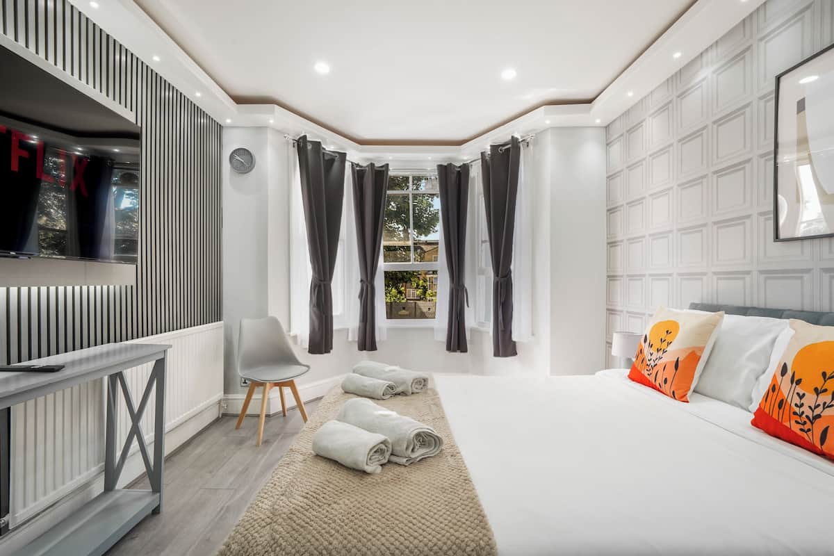 A modern hotel room with a bed, a desk, a chair, and a window with curtains.