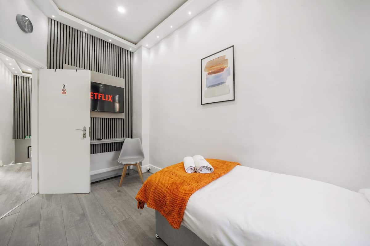 A modern hotel room with a bed, a TV, a door, and a wall-mounted artwork.