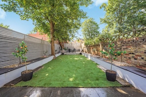 A backyard with a well-maintained lawn, two potted orange trees, a brick wall, and a wooden fence.