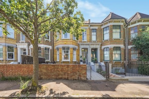 A row of terraced houses with a tree in the foreground, a gated entrance, and a brick wall. - The Cozy Stays Hackney House (London)