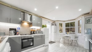 A modern kitchen with grey cabinets, a built-in oven, a coffee maker, and a water dispenser. - The Cozy Stays Hackney House (London)