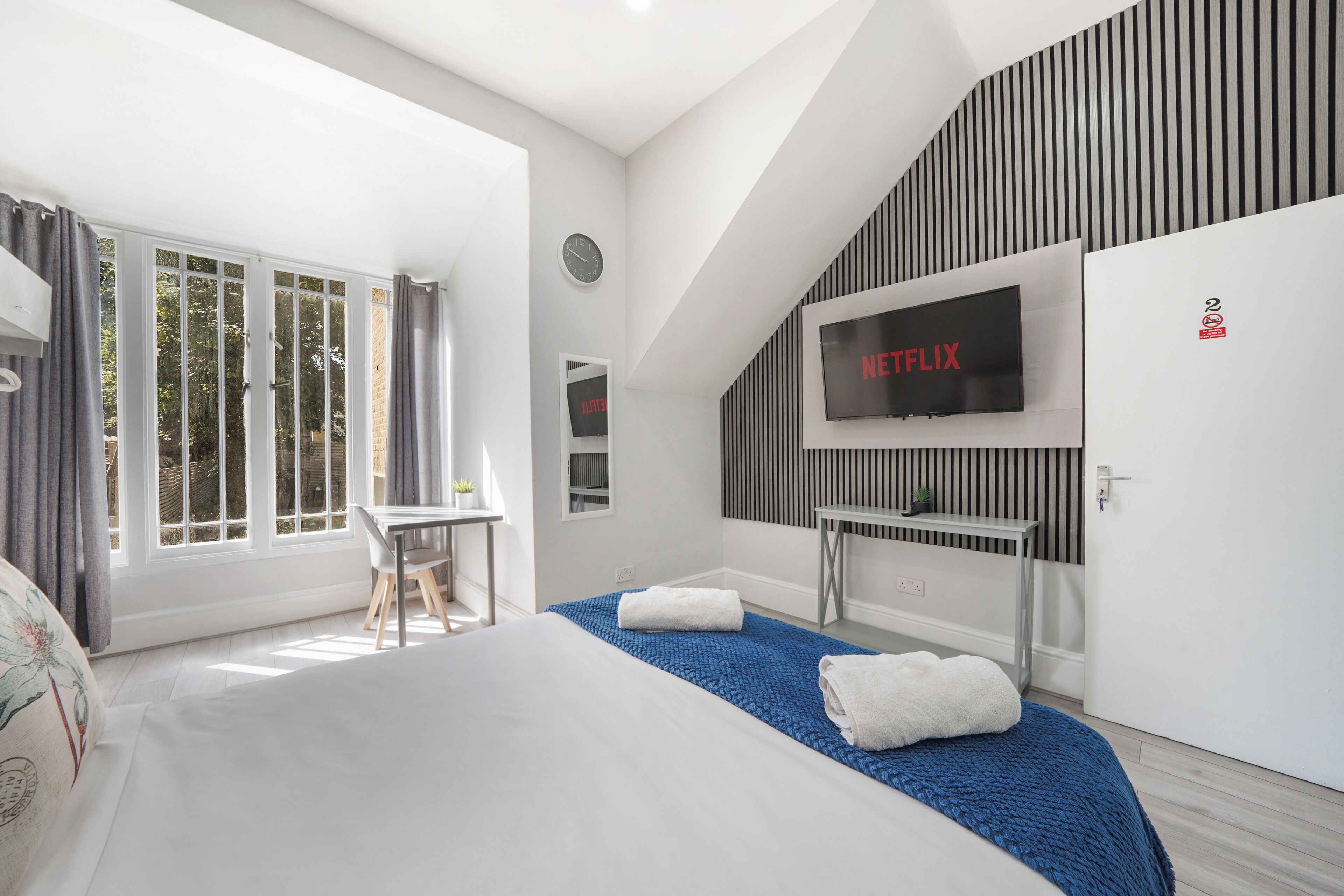 Une chambre d’hôtel moderne équipée d’un lit, d’un bureau, d’un téléviseur fixé au mur et d’une grande fenêtre.