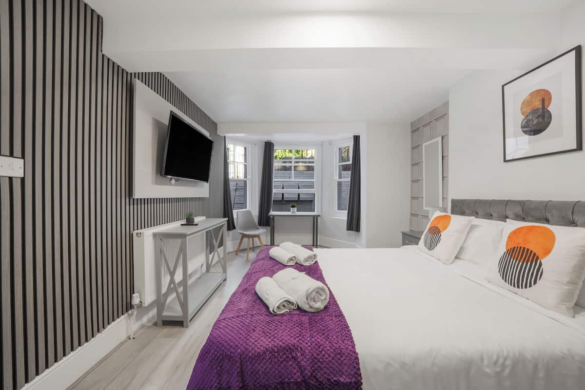 A modern hotel room with a bed, a desk, a TV, and a view of the outdoors.