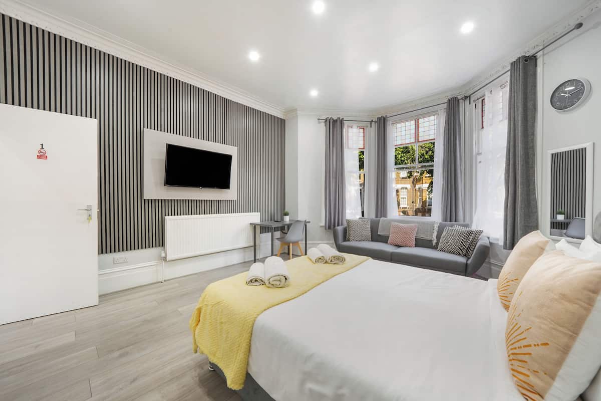 A hotel room with a bed, a TV, a sofa, a desk, and a window with curtains.