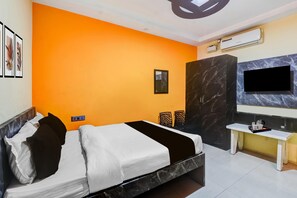 A hotel room with an orange accent wall, a bed with white and black bedding, a marble accent wall, a TV mounted on the wall, and a small table with a tray.