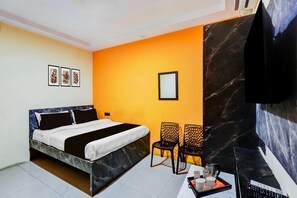 A bedroom with a bed, two chairs, a table with a tray, a remote control, and framed pictures on the wall.