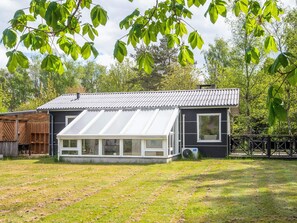 Ein eingeschossiges Haus mit einer großen Glasveranda, umgeben von einem Rasen und Bäumen.