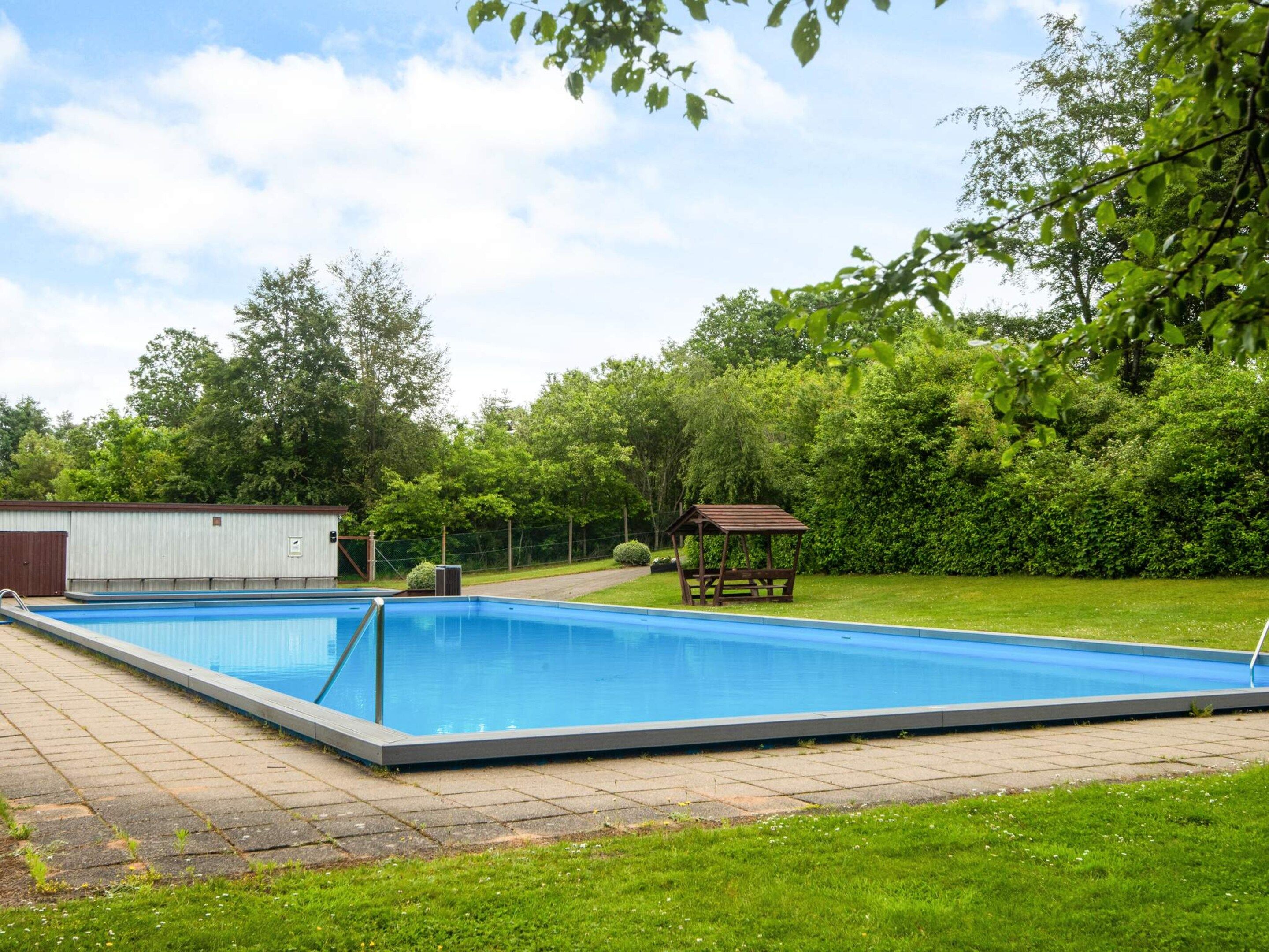 A rectangular swimming pool with a wooden deck surrounding it, a small shed, and a gazebo in a landscaped backyard.