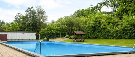 A rectangular swimming pool with a wooden deck surrounding it, a small shed, and a gazebo in a landscaped backyard.
