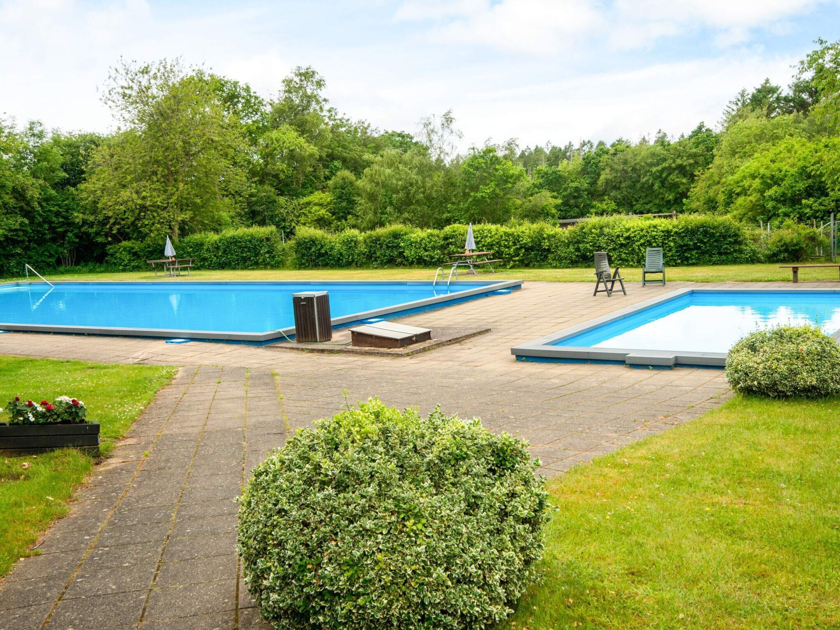 A swimming pool area with two pools, a pathway, and surrounding greenery.