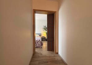 A hallway leading to a bedroom with a bed, bedside table, lamp, and a potted plant. - Pastelowo Gdańsk with Balcony & Free Parking (Gdańsk)