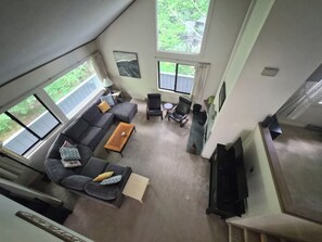 A living room with a sofa, coffee table, and a TV. There are windows and a ceiling fan. - Private, stand-alone, updated property, abuts woods, near Loon. C0146 by LRS (Lincoln)