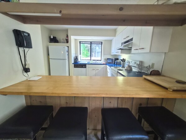 A kitchen with a wooden countertop, two black stools, a refrigerator, a microwave, and cabinets. - Private, stand-alone, updated property, abuts woods, near Loon. C0146 by LRS (Lincoln)