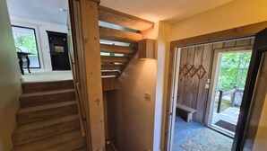 Eine Holztreppe führt zu einer zweiten Etage, eine Glastür bietet Blick ins Freie und eine kleine Bank steht draußen.