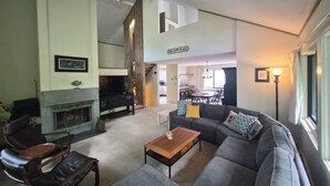 Ein Wohnzimmer mit Sofa, Couchtisch und Kamin. Im Hintergrund befindet sich ein Essbereich mit Tisch und Stühlen.