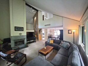 A living room with a sofa, coffee table, and fireplace. There is a dining area with a table and chairs in the background. - Private, stand-alone, updated property, abuts woods, near Loon. C0146 by LRS (Lincoln)