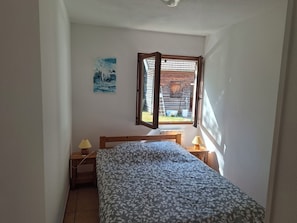 A bedroom with a bed, two bedside lamps, a window, and a painting on the wall.
