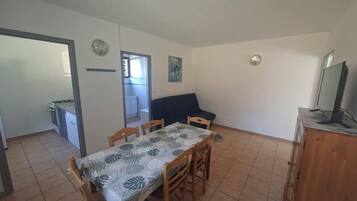 Een eetgedeelte met een tafel en stoelen, een kitchenette, een bank en een televisie op een houten kast.