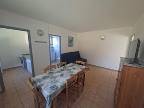 Ein Essbereich mit Tisch und Stühlen, einer Küchenzeile, einer Couch und einem Fernseher auf einer Holzkommode.