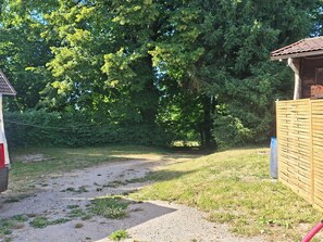 Ein Kiesweg führt zu einer Holzhütte mit Ziegeldach, umgeben von dichtem Grün.