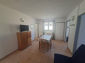 A room with a dining table, chairs, a TV on a wooden cabinet, and a door leading to another room.
