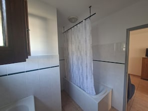 A bathroom with white tiles, a bathtub, a shower curtain, and a wooden cabinet.
