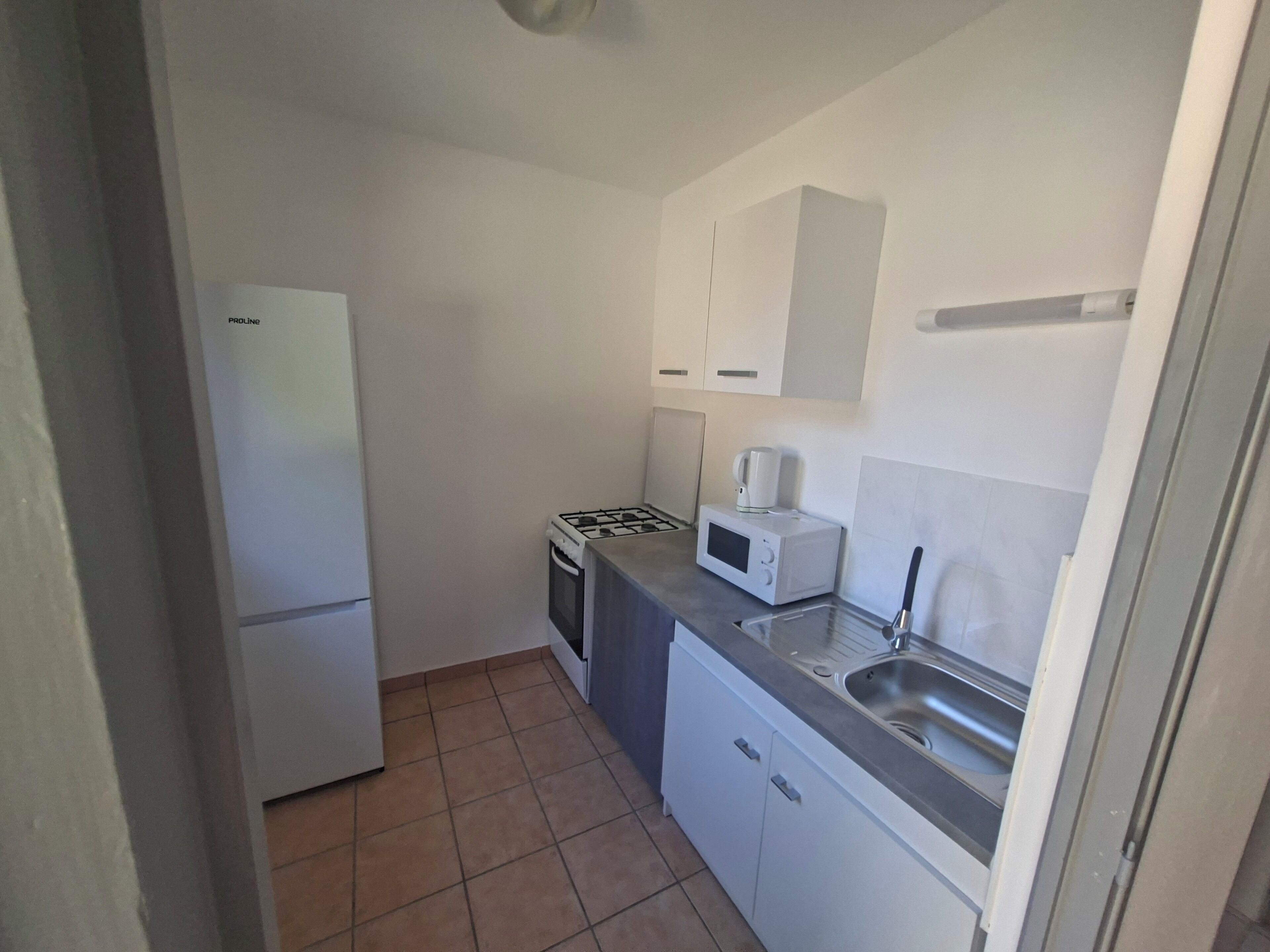 A compact kitchen with a refrigerator, stove, microwave, and sink.