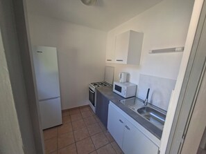 Eine kleine Küche mit Kühlschrank, Herd, Mikrowelle und Spüle.
