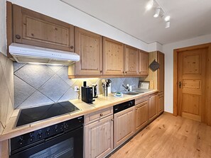 A modern kitchen with wooden cabinets, a built-in stove, and a dishwasher. - Nendaz 4 Vallées | Sauna | Parking | Cosy Escape (Haute-Nendaz)