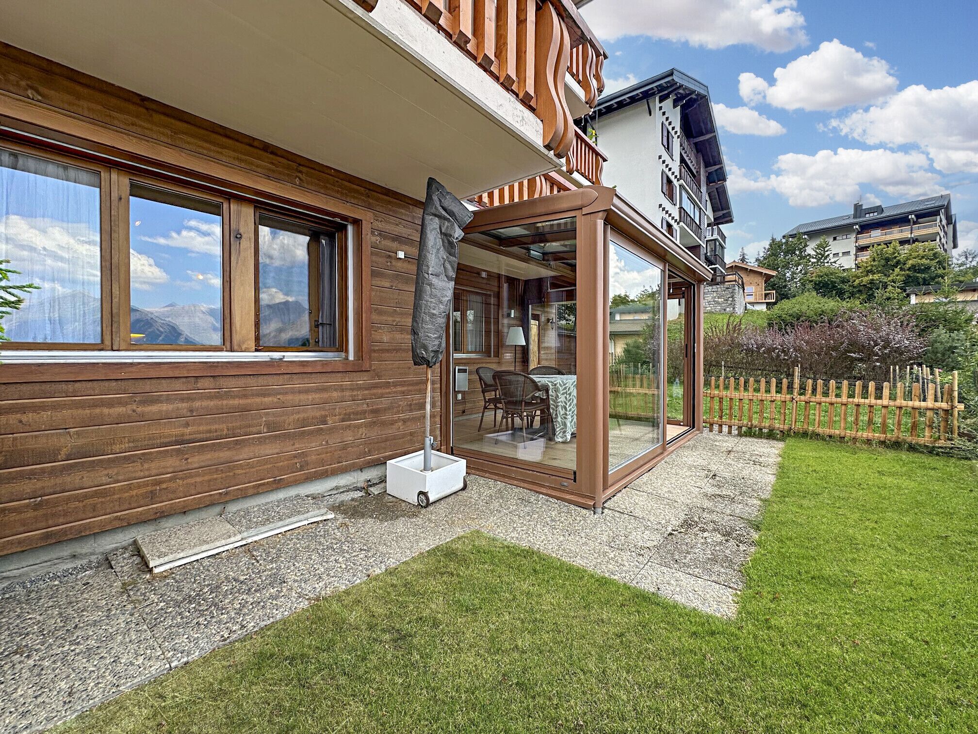 A modern house with a wooden facade, large windows, and a glass door leading to a patio.