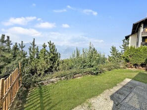 A residential area with a paved driveway, a wooden fence, and a variety of trees including conifers and shrubs. - Nendaz 4 Vallées | Sauna | Parking | Cosy Escape (Haute-Nendaz)