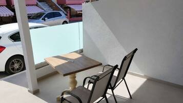 Uma varanda com mesa e cadeiras, com vista para uma rua com carros estacionados e edifícios.