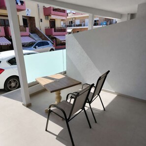 Ein Balkon mit Tisch und Stühlen, der auf eine Straße mit parkenden Autos und Gebäuden blickt.