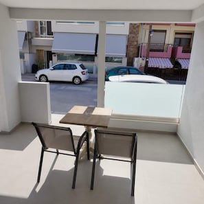 Ein Balkon mit Tisch und Stühlen, Blick auf geparkte Autos und Gebäude im Hintergrund.