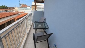 Ein Balkon mit Tisch und Stühlen, ein Fliesenboden und Blick auf Gebäude im Hintergrund.