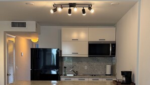 A modern kitchen with a black refrigerator, stainless steel microwave, and a built-in oven. There are two bar stools and a coffee maker on the counter. - Perfect 1-bedroom apartment with AC and free parking in North Bay Village (North Bay Village)