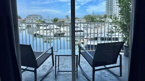 A balcony with two chairs and a table, overlooking a marina with boats and buildings. - Perfect 1-bedroom apartment with AC and free parking in North Bay Village (North Bay Village)