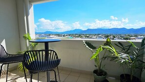 A balcony with a table and chairs, potted plants, and a view of a cityscape and mountains. - Tropical Sunsets Studio with rooftop pool in Cairns City (Cairns City)