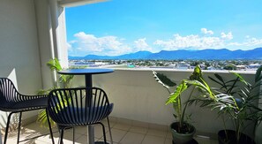 A balcony with a table and chairs, potted plants, and a view of a cityscape and mountains. - Tropical Sunsets Studio with rooftop pool in Cairns City (Cairns City)