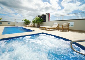 Una piscina en la azotea con hidromasaje, sillas de descanso y plantas en macetas.