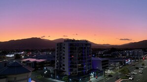 A multi-story building with a flat roof, surrounded by other buildings and a road with vehicles. - Tropical Sunsets Studio with rooftop pool in Cairns City (Cairns City)