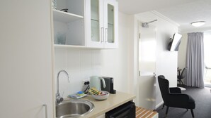 A compact kitchenette with a microwave, sink, and a small refrigerator. There is a chair and a table in the adjacent living area. - Tropical Sunsets Studio with rooftop pool in Cairns City (Cairns City)