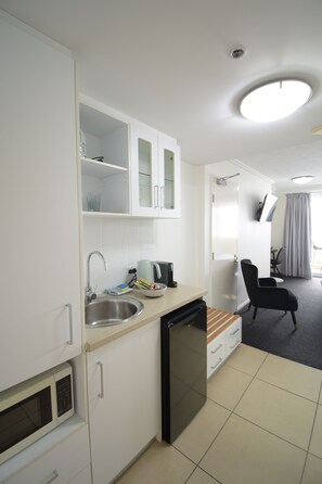 A compact kitchenette with a microwave, sink, and a small refrigerator. There is a chair and a table in the adjacent living area. - Tropical Sunsets Studio with rooftop pool in Cairns City (Cairns City)
