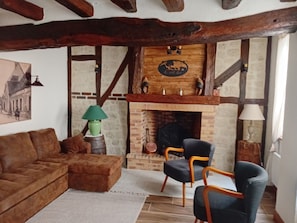 Ein gemütliches Wohnzimmer mit Kamin, Holzbalken, einer Couch, zwei Sesseln und einer Lampe.