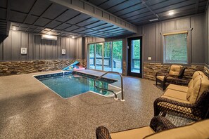 A spa area with a hot tub, stone wall, wicker furniture, and a view of the outdoors. - Mountain Creek Oasis | Private Heated Indoor Pool + Hot Tub (Sevierville)
